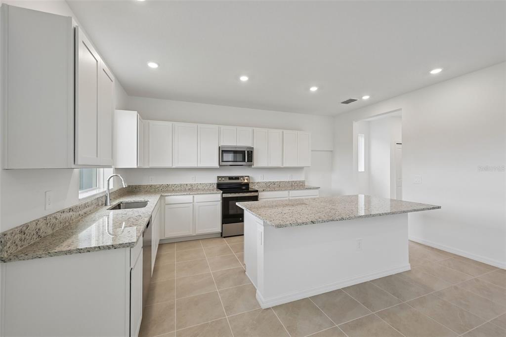 A kitchen features white cabinets, granite countertops, stainless steel appliances, and a central island — 4508 OUTHAUL RUN, PALMETTO, FL