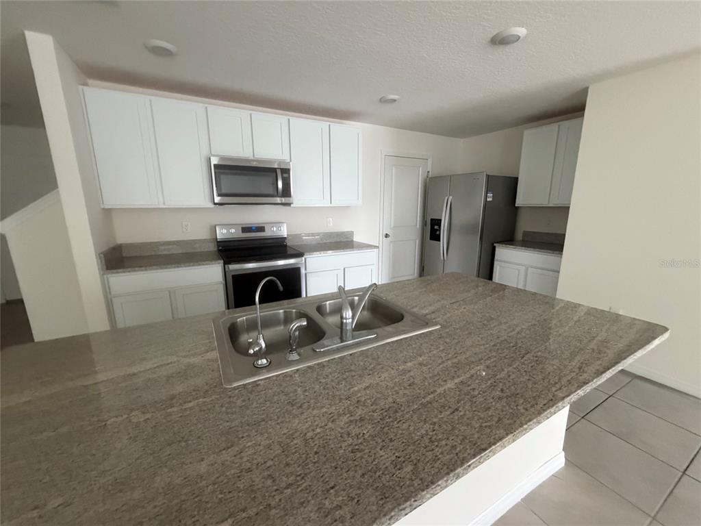 A kitchen features white cabinets, granite countertops, stainless steel appliances, and a central island sink — 12153 WHITE CYPRESS PLACE, RIVERVIEW, FL