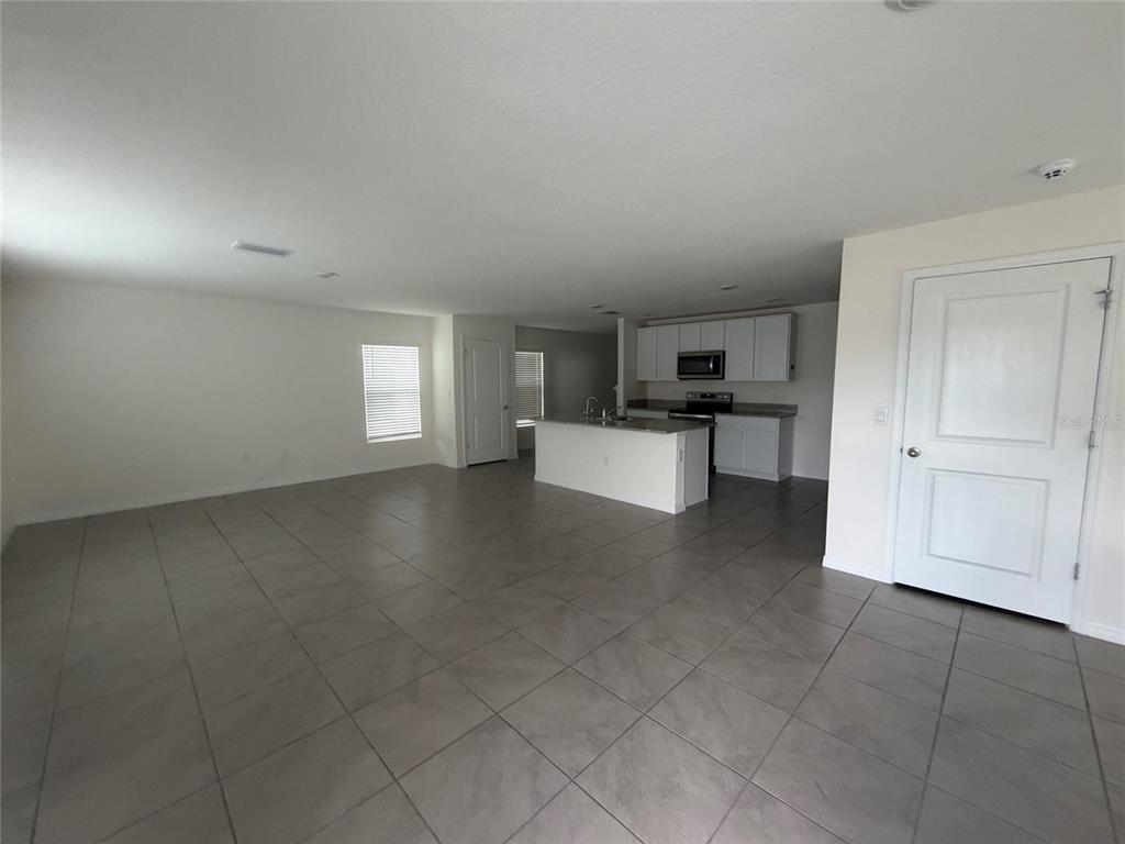 An open-concept living area features gray tile flooring, a kitchen island, and white cabinetry — 12153 WHITE CYPRESS PLACE, RIVERVIEW, FL