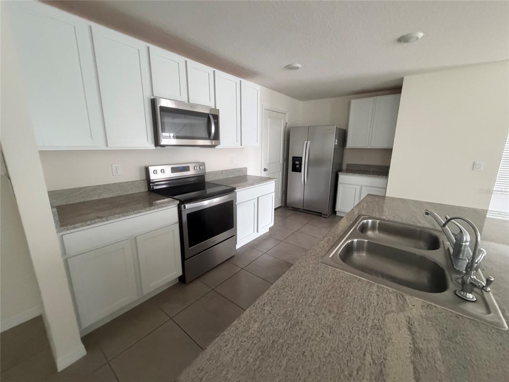 A kitchen features white cabinets, stainless steel appliances, and a granite-topped island with a sink — 12153 WHITE CYPRESS PLACE, RIVERVIEW, FL