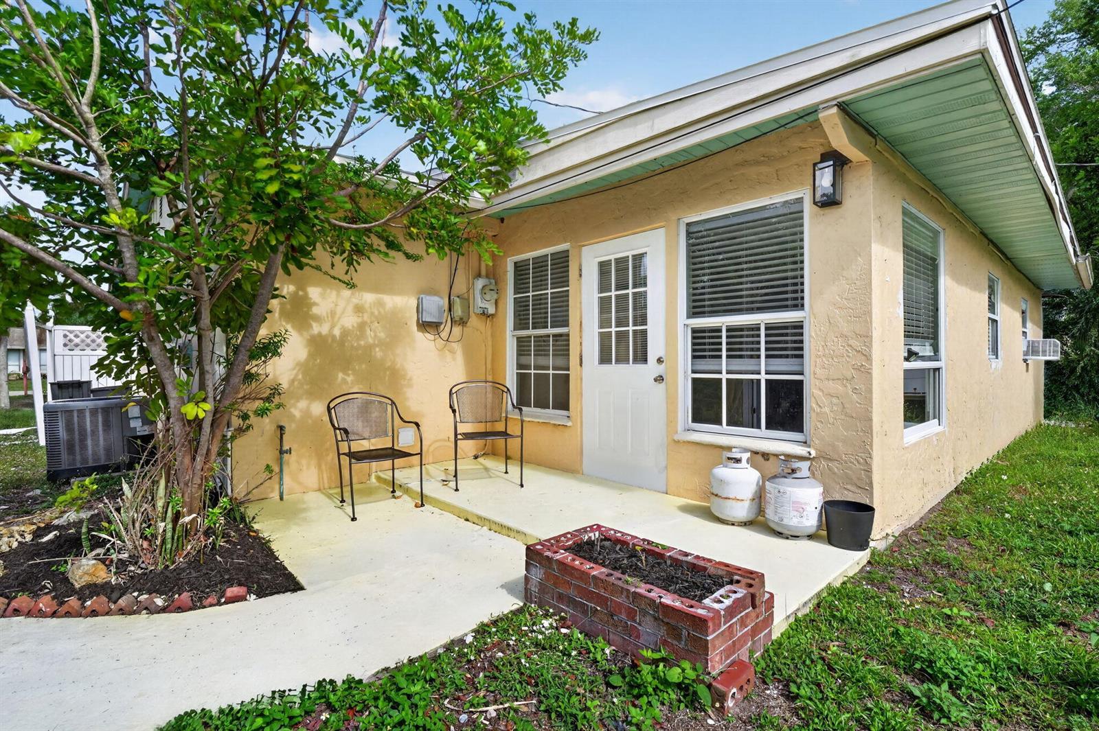 A yellow house exterior features a concrete patio, two chairs, and a brick planter box — 1934 Flamingo Drive, FL 33917, FL