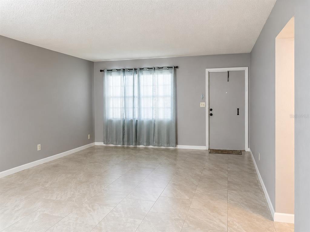An empty room with gray walls, tile flooring, and a window with sheer curtains — 400 AUBURN DRIVE UNIT 3, DAYTONA BEACH, FL