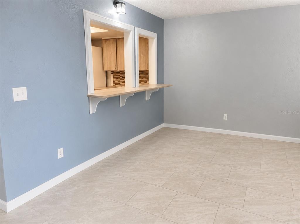 A room with light-colored tile flooring, gray walls, and a kitchen pass-through window with a counter — 400 AUBURN DRIVE UNIT 3, DAYTONA BEACH, FL