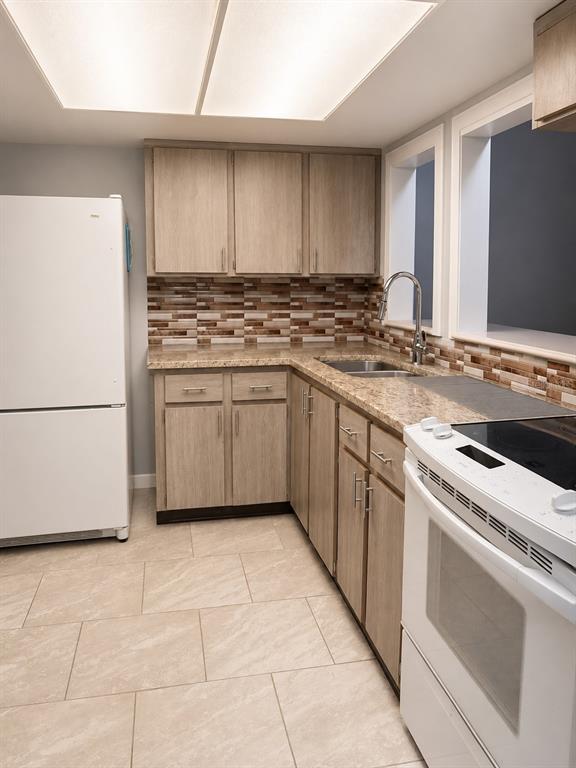 A kitchen features light wood cabinets, granite countertops, a tiled backsplash, and white appliances — 400 AUBURN DRIVE UNIT 3, DAYTONA BEACH, FL