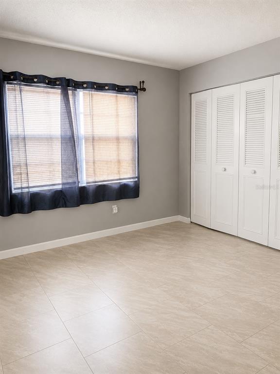 A bedroom with gray walls, tile flooring, a window with dark curtains, and white closet doors — 400 AUBURN DRIVE UNIT 3, DAYTONA BEACH, FL