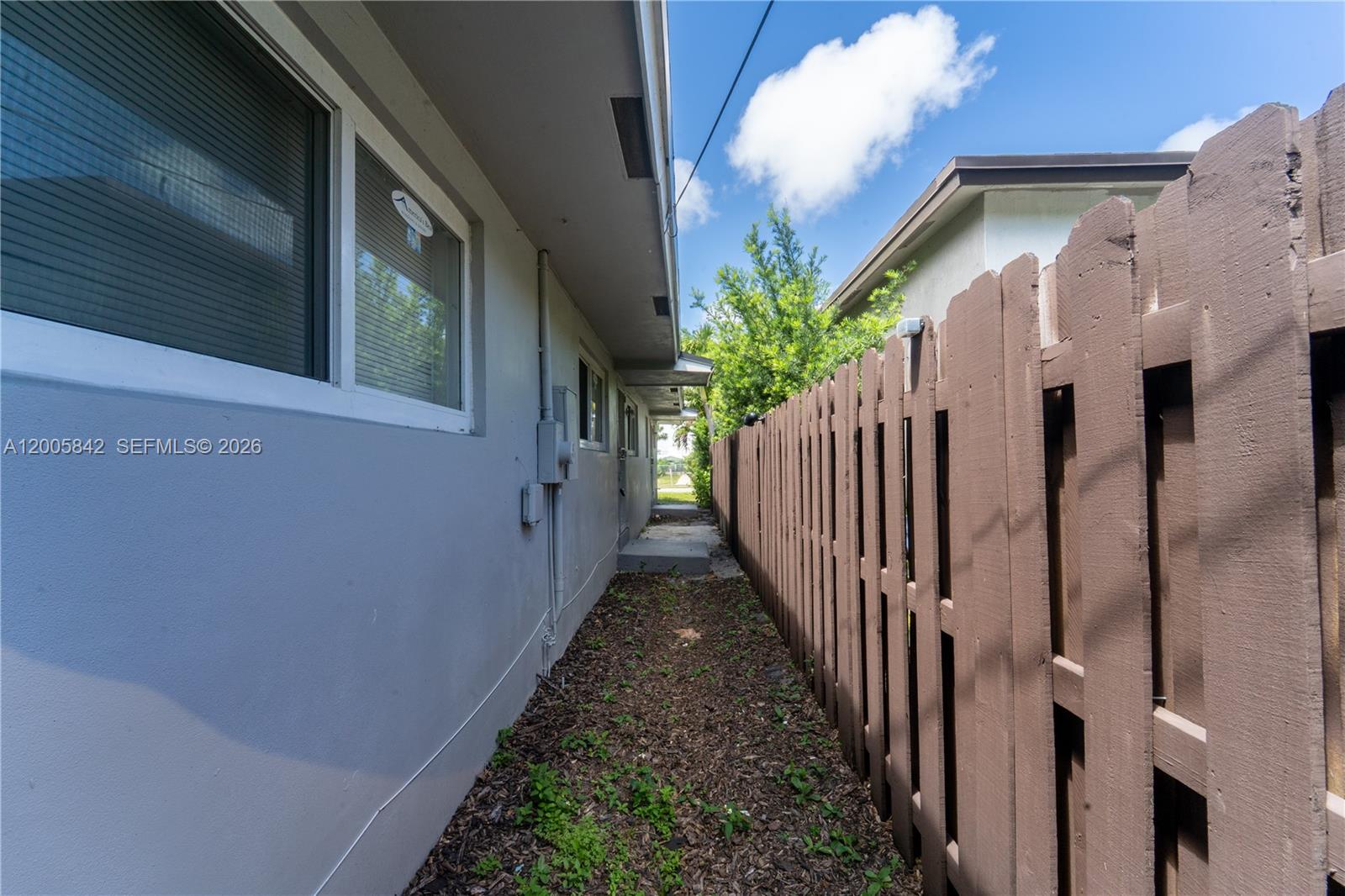 A narrow side yard features a gray house wall, a brown wooden fence, and mulch — 2260 Charleston St, Hollywood FL 33020, HOLLYWOOD, FL