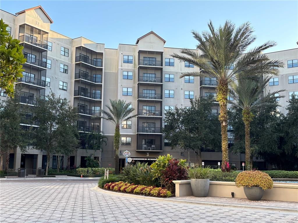 A multi-story apartment building with balconies and palm trees stands behind a landscaped circular driveway — 14501 GROVE RESORT AVENUE UNIT 3304, WINTER GARDEN, FL