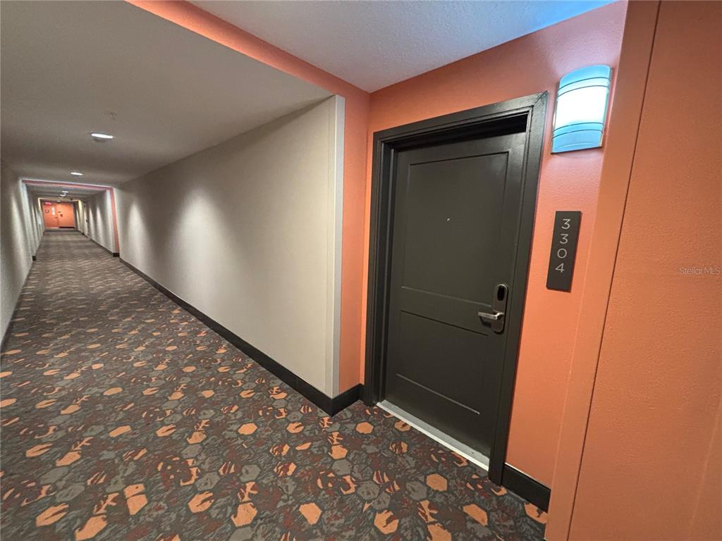 A dark door labeled 3304 sits in a long hallway with patterned carpet and orange walls — 14501 GROVE RESORT AVENUE UNIT 3304, WINTER GARDEN, FL