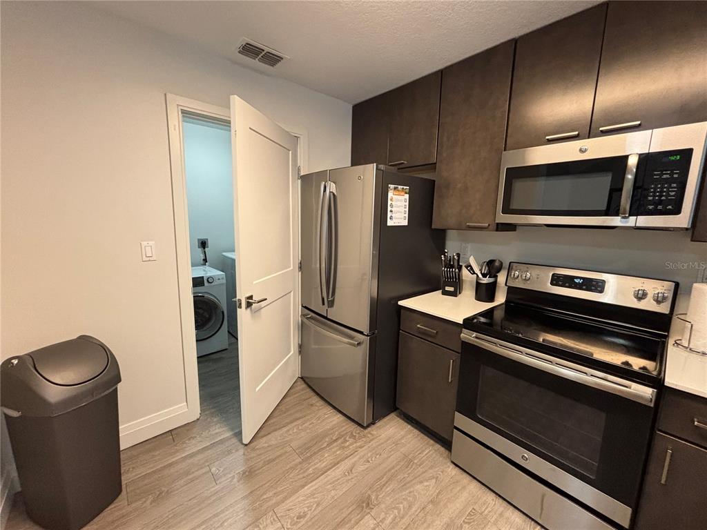 A kitchen features stainless steel appliances, dark wood cabinets, and a doorway leading to laundry — 14501 GROVE RESORT AVENUE UNIT 3304, WINTER GARDEN, FL