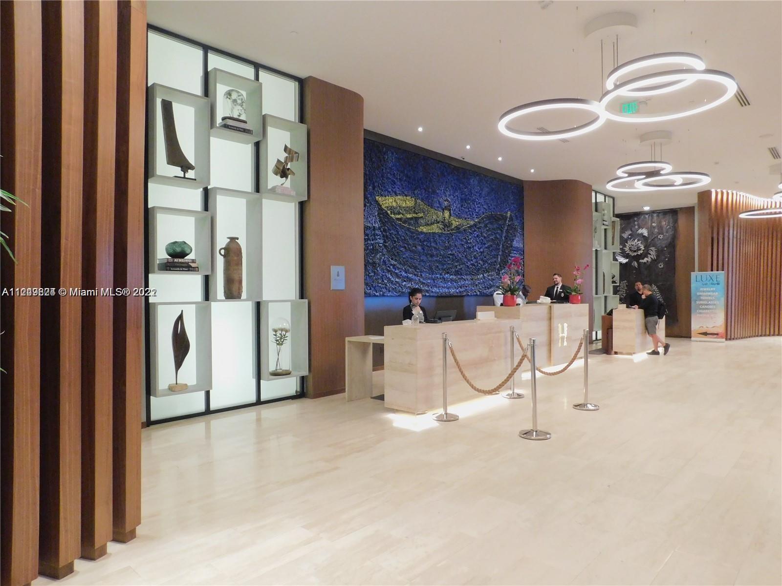 A hotel lobby features a reception desk, decorative shelving, and modern circular light fixtures — 4111 S Ocean Dr # 1004, Hollywood FL 33019, HOLLYWOOD, FL