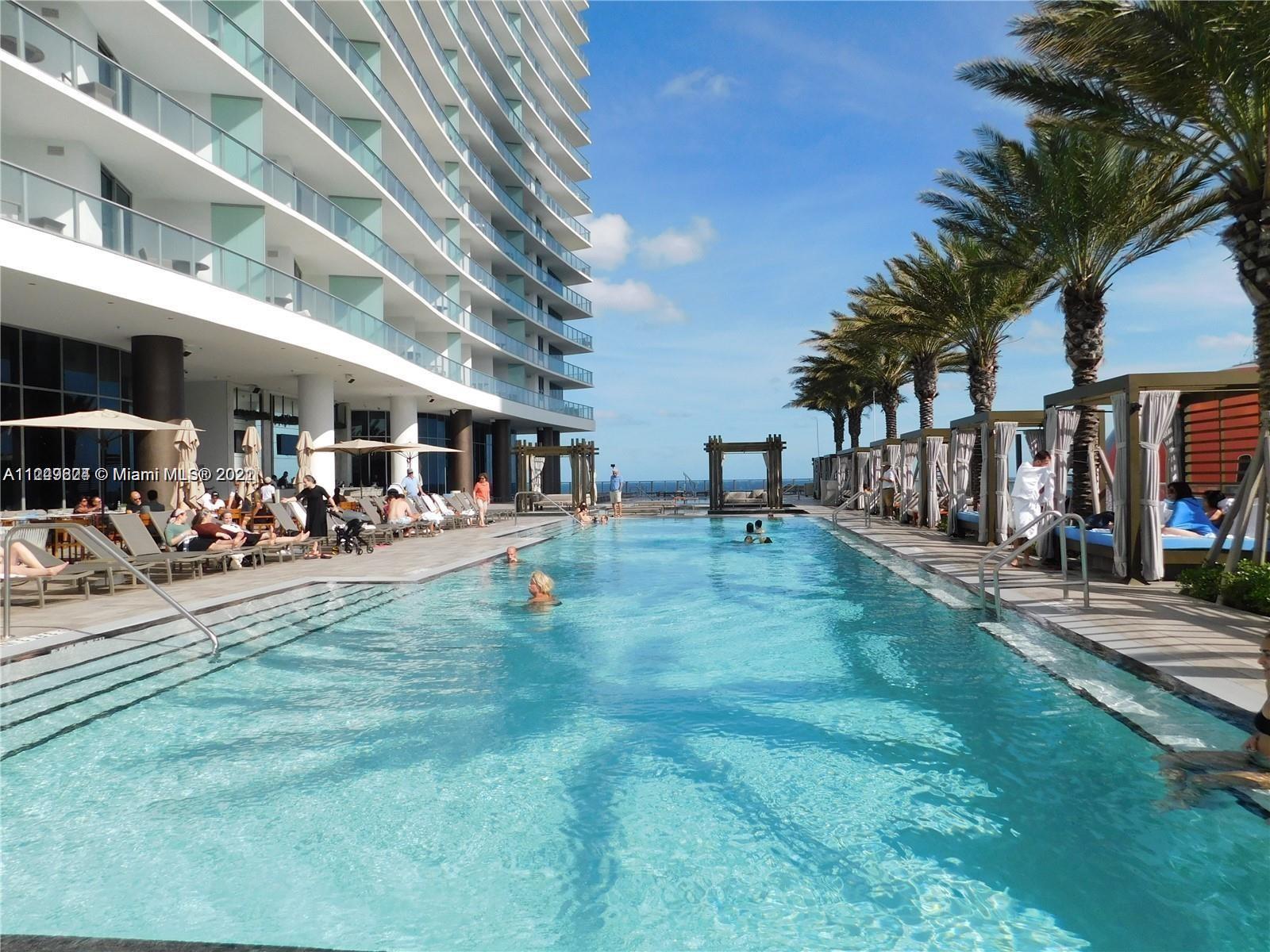 A long swimming pool sits beside a modern high-rise building with poolside cabanas and palm trees — 4111 S Ocean Dr # 1004, Hollywood FL 33019, HOLLYWOOD, FL