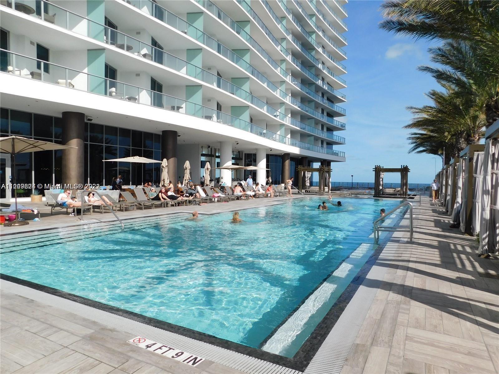 A large outdoor swimming pool sits beside a modern multi-story building with glass balconies — 4111 S Ocean Dr # 1004, Hollywood FL 33019, HOLLYWOOD, FL