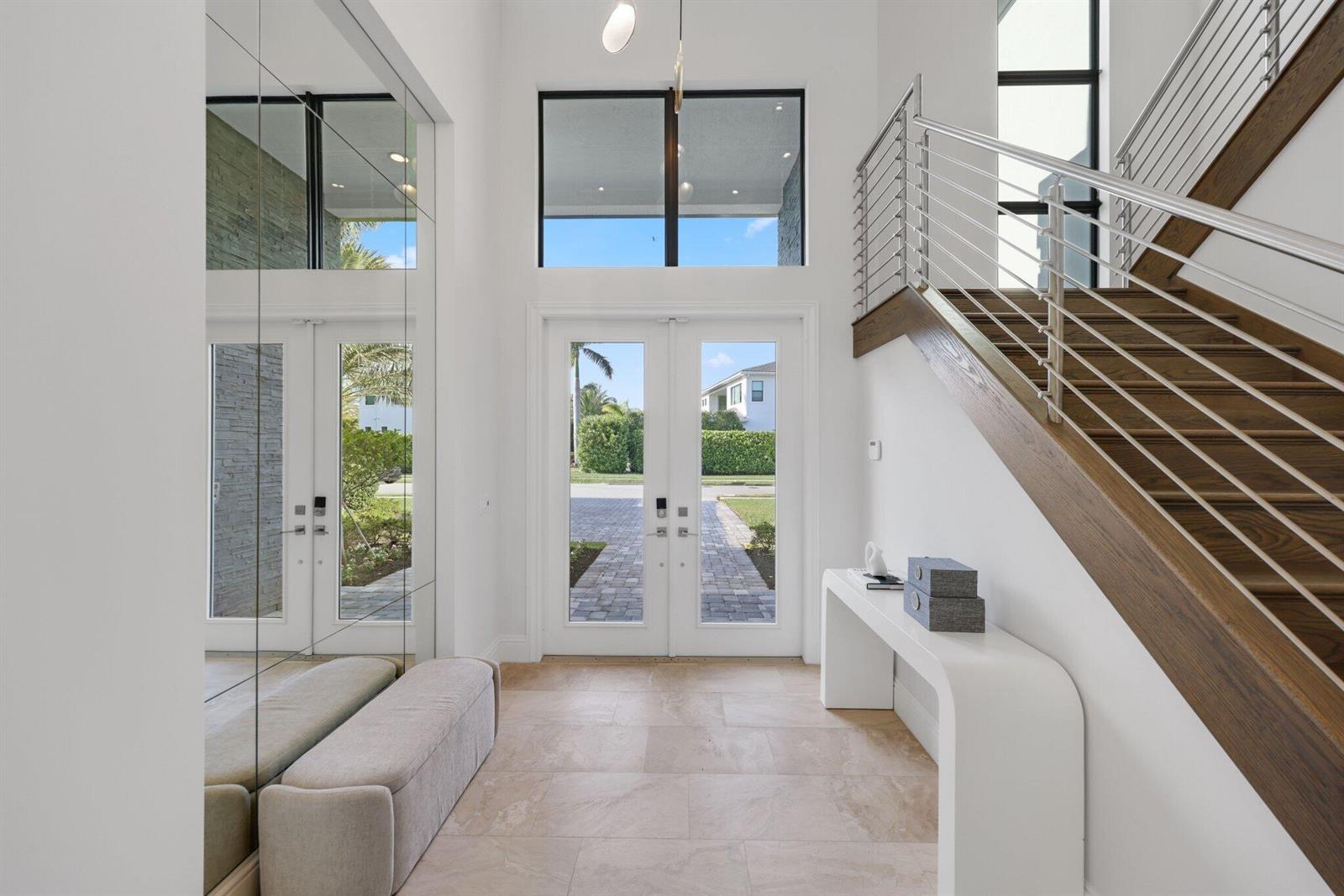 A bright entryway features a staircase with wood treads, a white console table, and mirrors — 2702 NW 71st Boulevard, Boca Raton FL 33496, BOCA RATON, FL