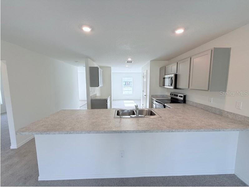 A kitchen features a peninsula with a sink, grey cabinets, and light-colored countertops — 25 ROUND THORN DRIVE, PALM COAST, FL