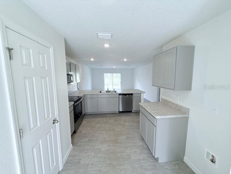 A kitchen with grey cabinets, stainless steel appliances, light countertops, and grey tile flooring — 25 ROUND THORN DRIVE, PALM COAST, FL