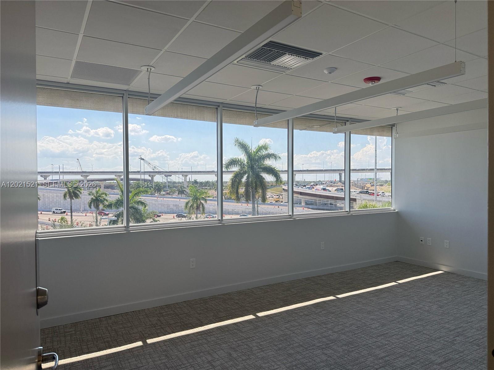 An empty office with gray carpet, white walls, and large windows overlooking a highway — 290 NW 165th St # 5C, Miami FL 33169, MIAMI, FL