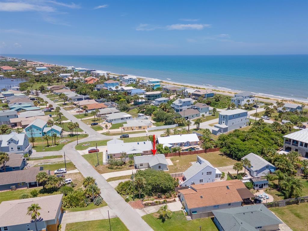 An aerial view shows a coastal neighborhood with a red arrow pointing to a house — 1956 N DAYTONA AVENUE, FLAGLER BEACH, FL