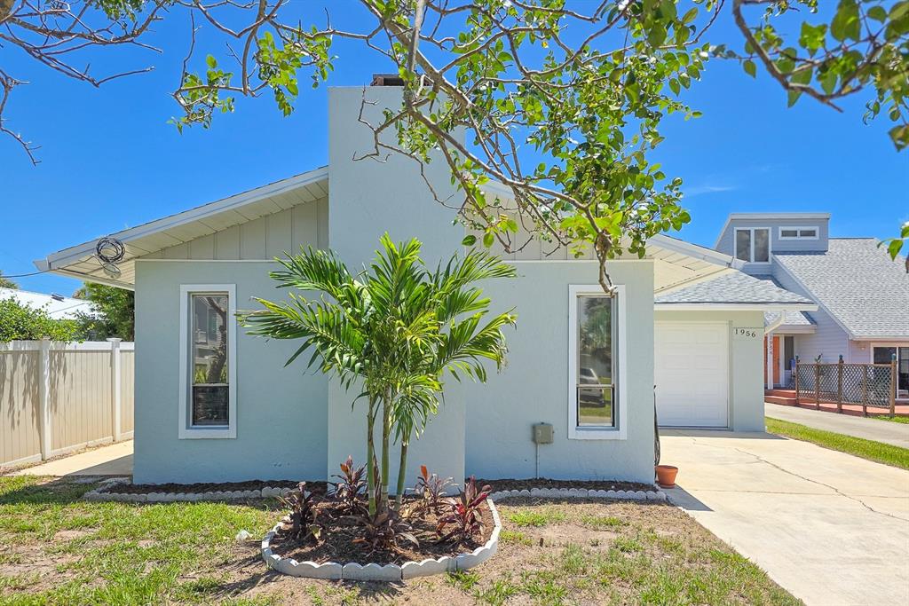 A light green single-story house features a central chimney, two tall windows, and a palm tree — 1956 N DAYTONA AVENUE, FLAGLER BEACH, FL