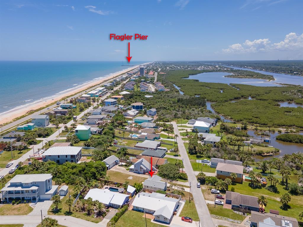 An aerial view shows a coastal neighborhood with houses, a beach, and the Flagler Pier — 1956 N DAYTONA AVENUE, FLAGLER BEACH, FL