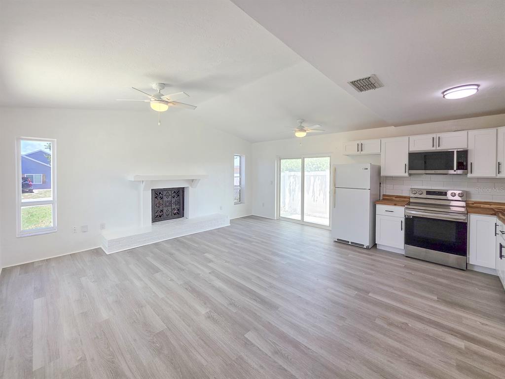 An open-concept living area features a white fireplace, light wood-look flooring, and a modern kitchen — 1956 N DAYTONA AVENUE, FLAGLER BEACH, FL