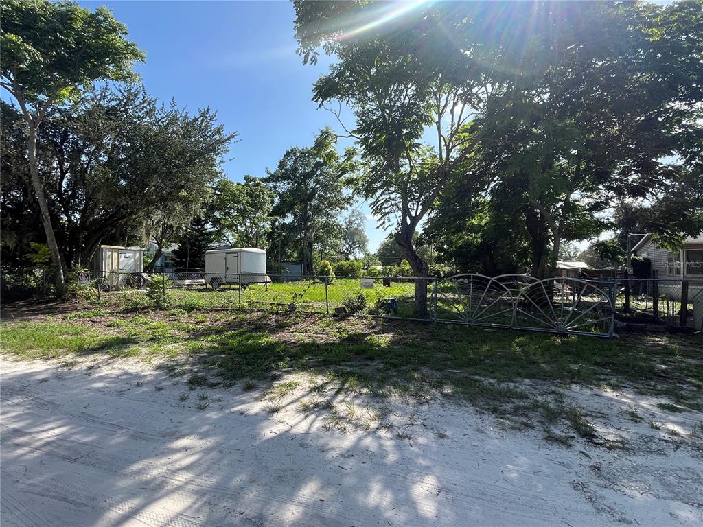 A fenced, grassy vacant lot is shaded by several large trees along a sandy road — 9315 KISSIMMEE ST, NEW PORT RICHEY, FL