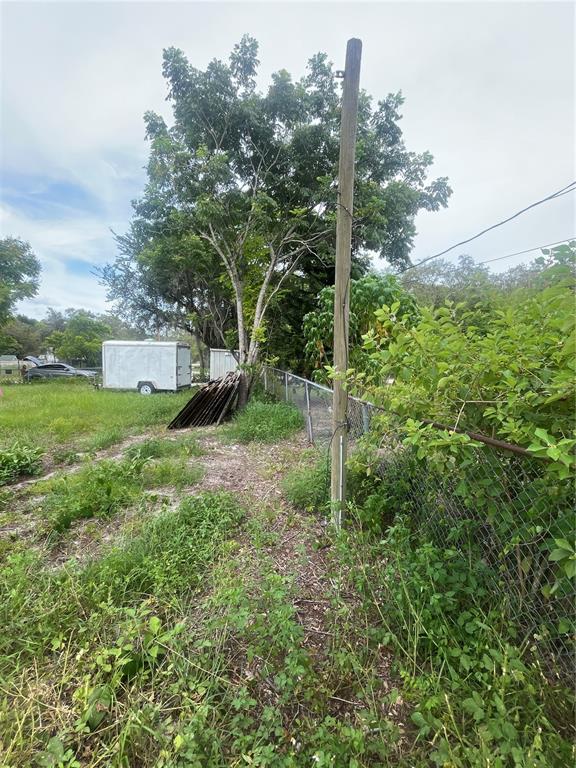 A wooden utility pole stands next to a chain-link fence in a grassy, overgrown lot — 9315 KISSIMMEE ST, NEW PORT RICHEY, FL