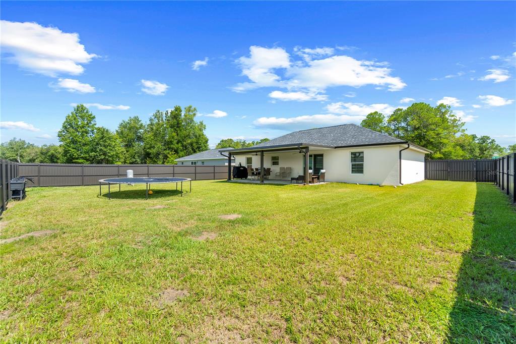 The backyard features a grassy lawn, a trampoline, and a covered patio attached to the house — 13210 SW 112TH PLACE, DUNNELLON, FL