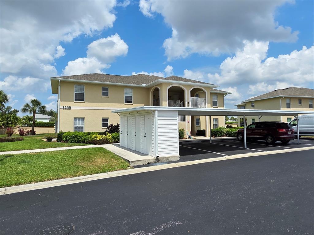 A two-story apartment building features a tan exterior, a white carport, and a parking lot — 5800 SABAL TRACE DRIVE UNIT 1201, NORTH PORT, FL