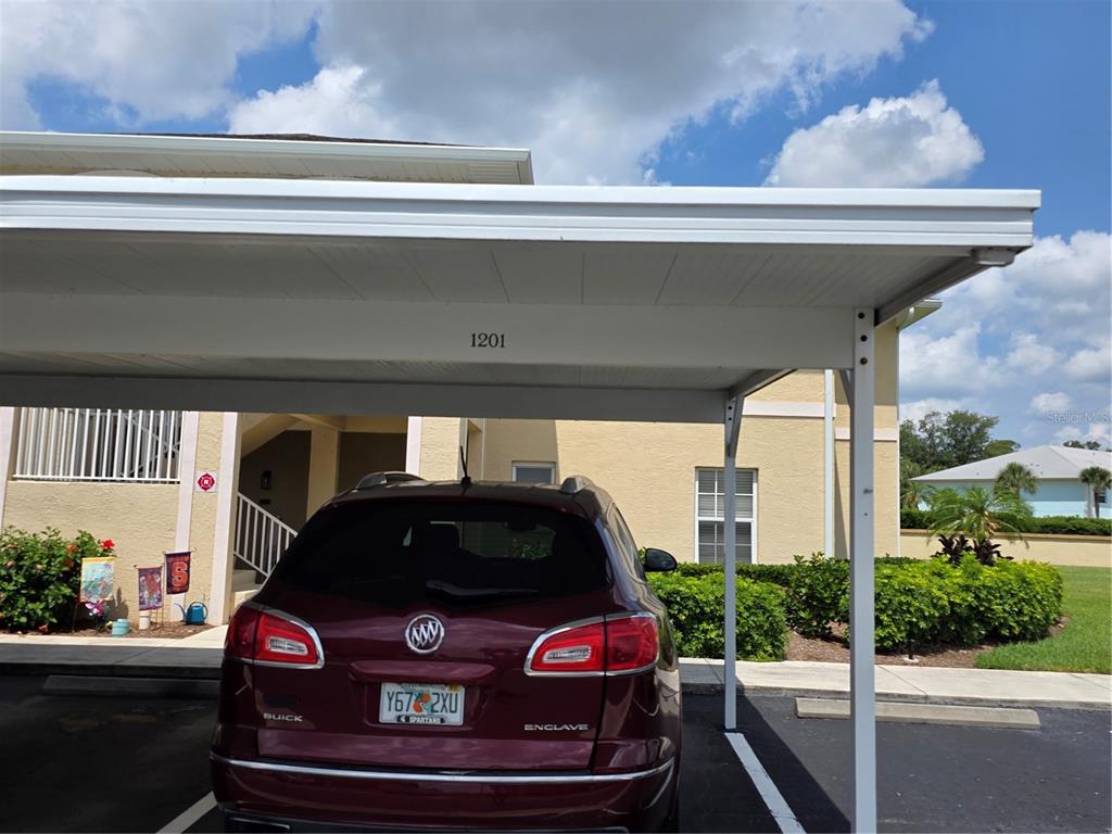 A maroon Buick Enclave is parked under a covered carport in front of a building — 5800 SABAL TRACE DRIVE UNIT 1201, NORTH PORT, FL