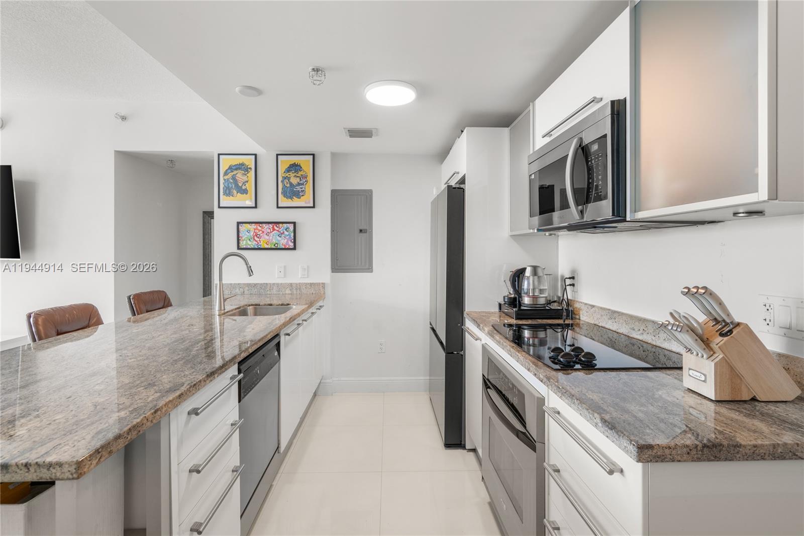 A modern kitchen features white cabinetry, granite countertops, stainless steel appliances, and tile flooring — 185 SW 7th St # 2702, Miami FL 33130, MIAMI, FL