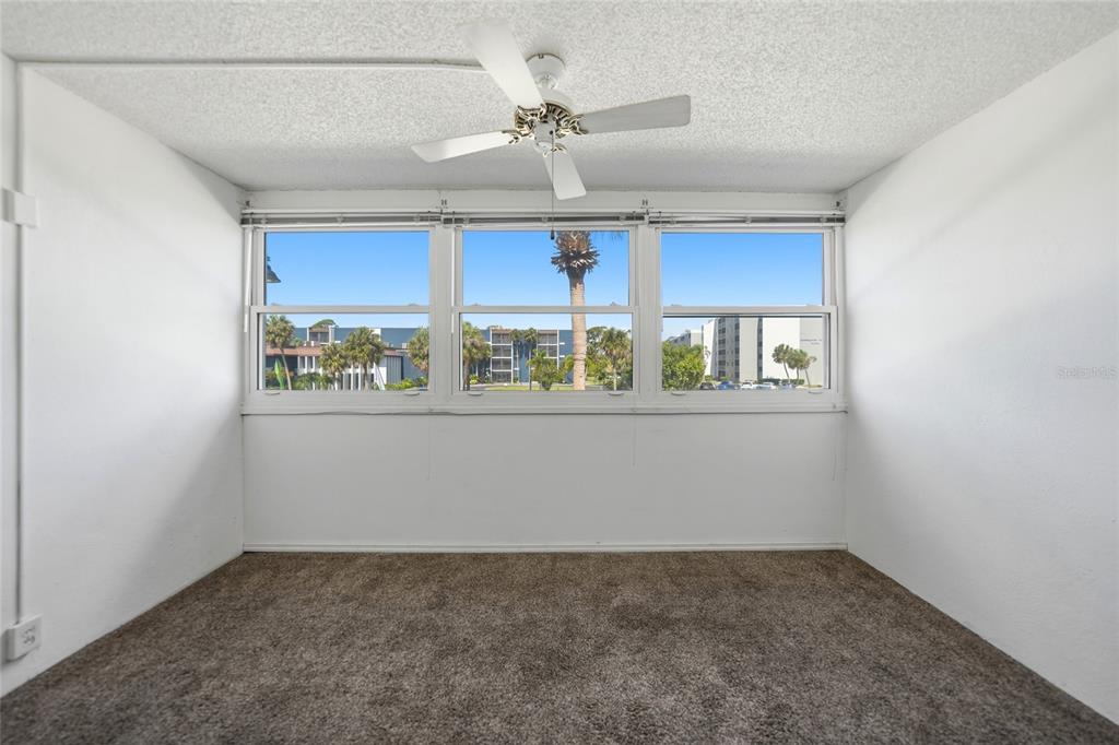An empty room with brown carpet, white walls, a ceiling fan, and three large windows — 2300 AARON STREET UNIT 204, PORT CHARLOTTE, FL