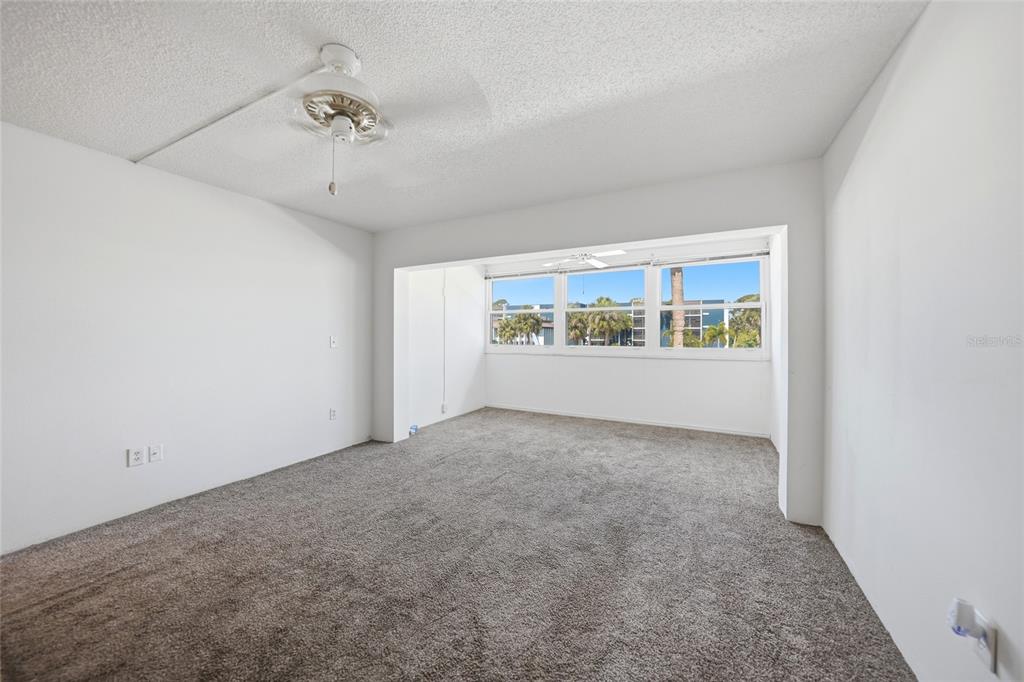 An empty bedroom features white walls, gray carpeting, a ceiling fan, and a large window — 2300 AARON STREET UNIT 204, PORT CHARLOTTE, FL