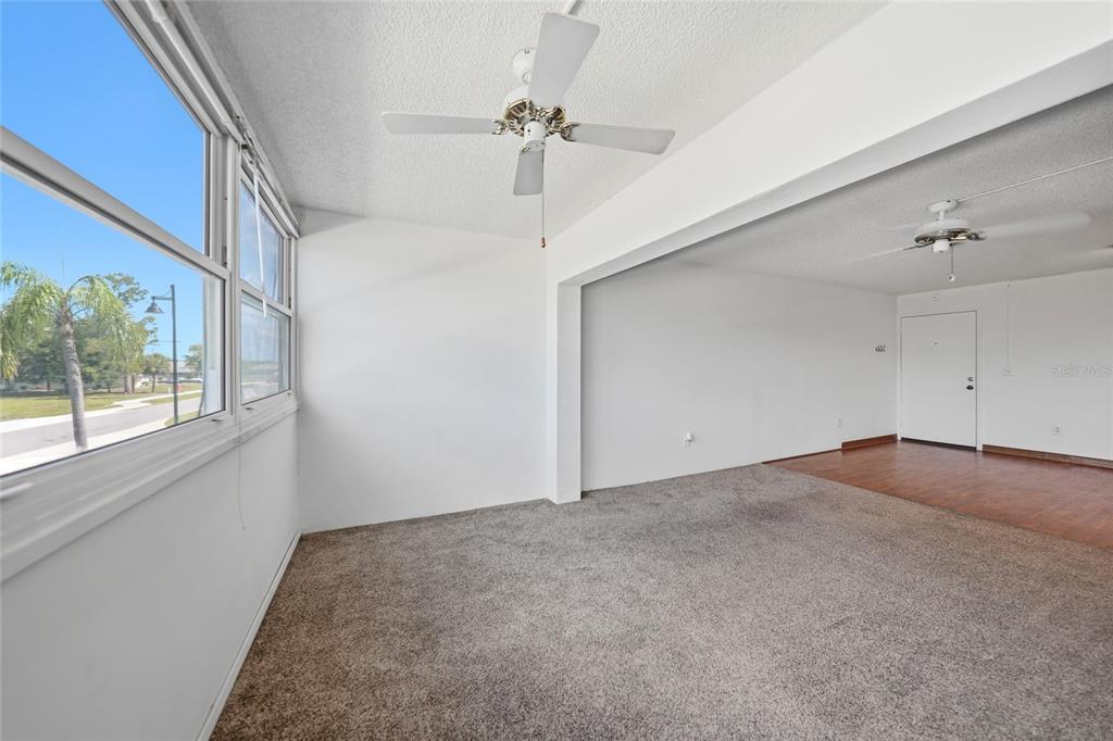 A carpeted sunroom with a ceiling fan connects to a living area with wood flooring — 2300 AARON STREET UNIT 204, PORT CHARLOTTE, FL