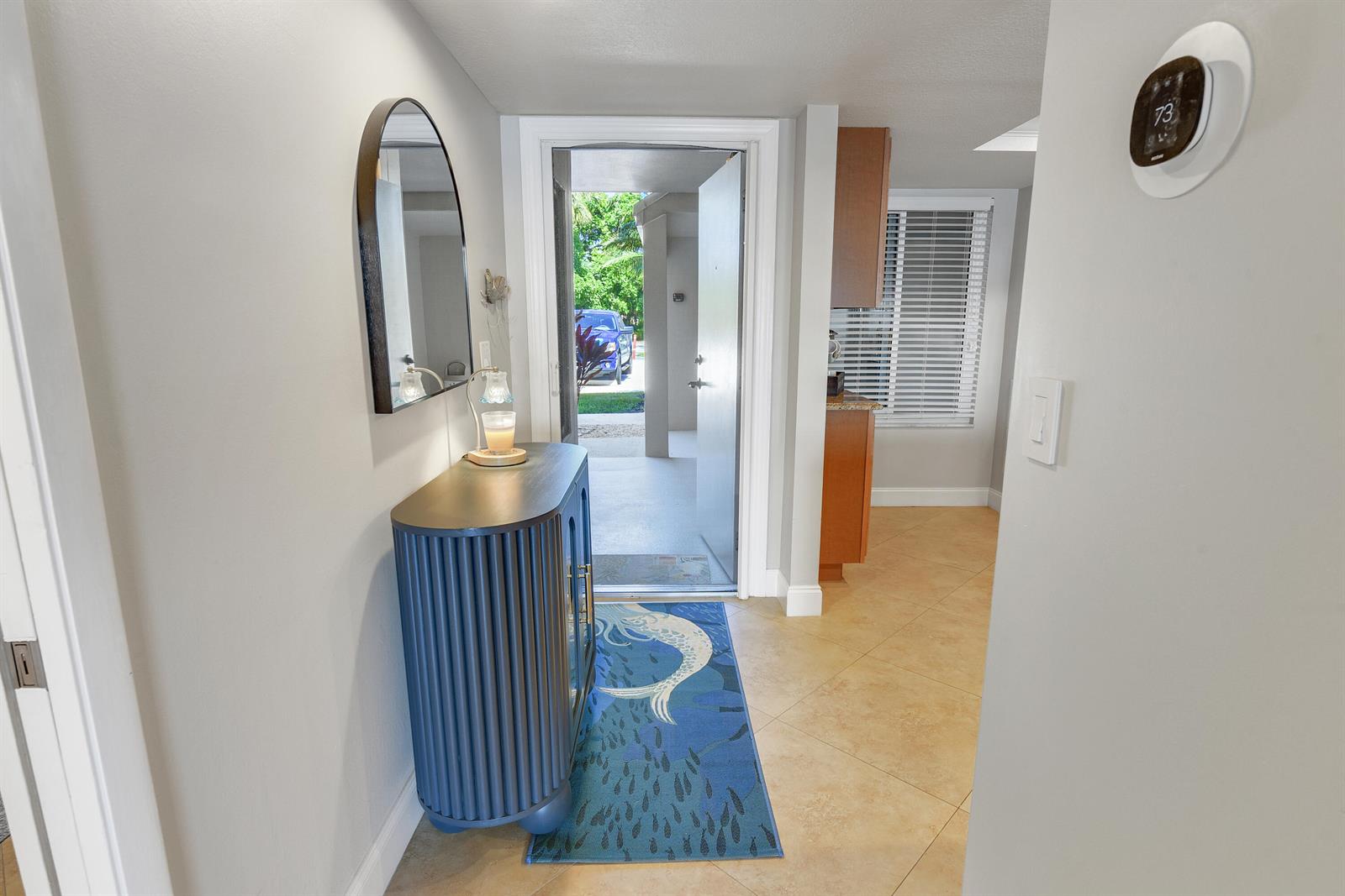 An entryway features a blue cabinet, a mirror, a fish-patterned rug, and an open door — 4440 NE Sandpebble Trace # 104, Stuart FL 34996, STUART, FL