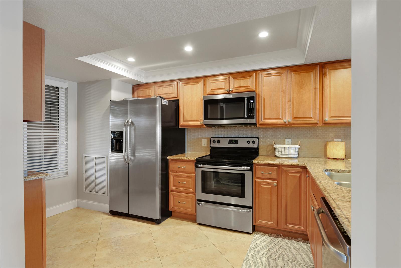 A kitchen features wood cabinets, stainless steel appliances, granite countertops, and tile flooring — 4440 NE Sandpebble Trace # 104, Stuart FL 34996, STUART, FL