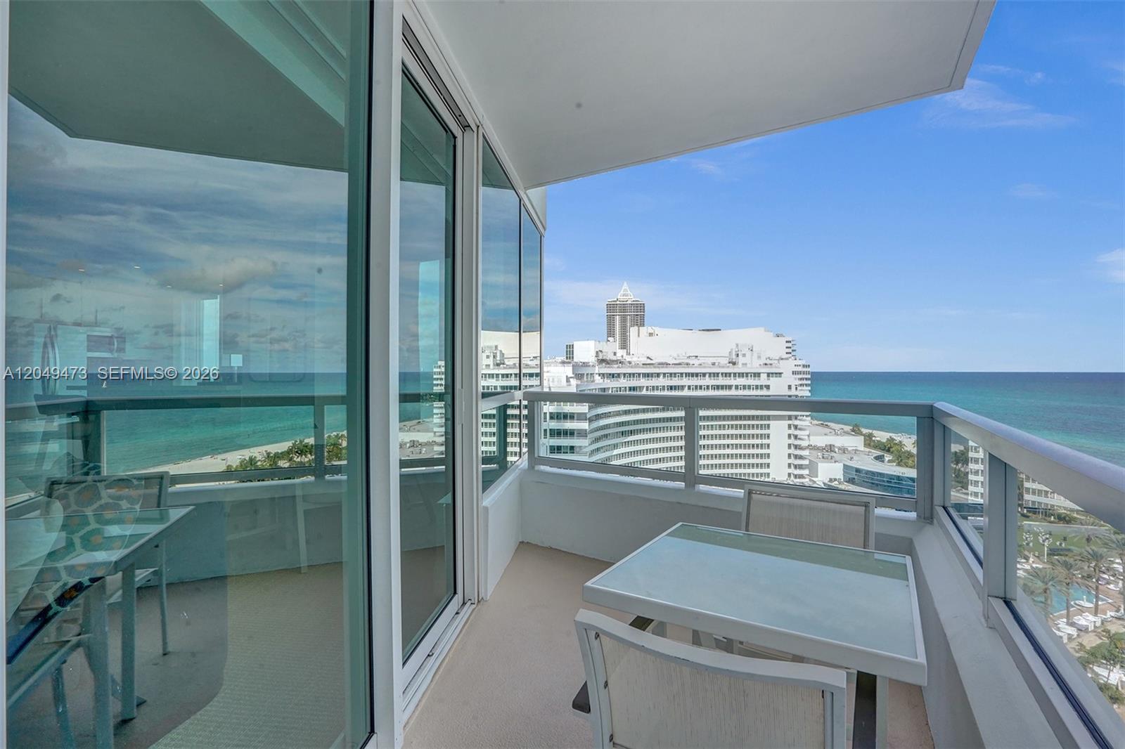 A balcony with a glass-topped table and chairs overlooks the ocean and nearby buildings — 4401 Collins Ave # 1503, Miami Beach FL 33140, MIAMI BEACH, FL