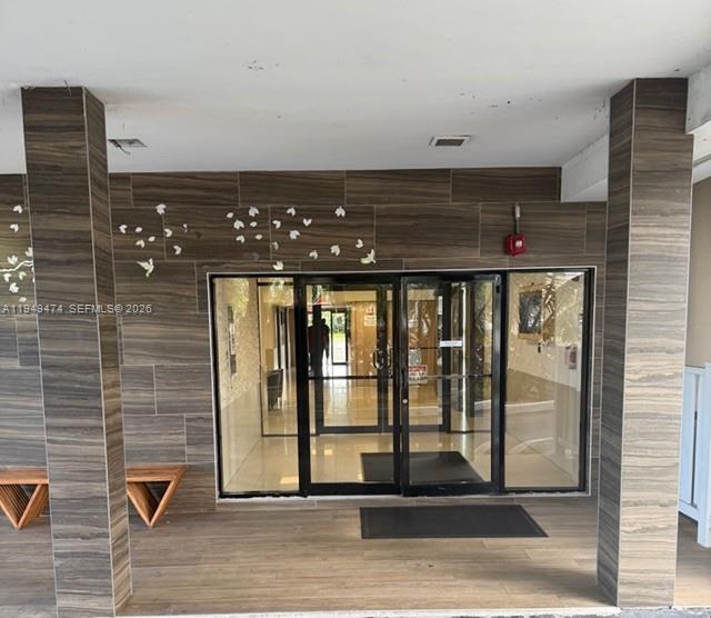The entrance to a building features glass double doors, wood-look tile walls, and two benches — 4164 Inverrary Dr # 913, Lauderhill FL 33319, LAUDERHILL, FL