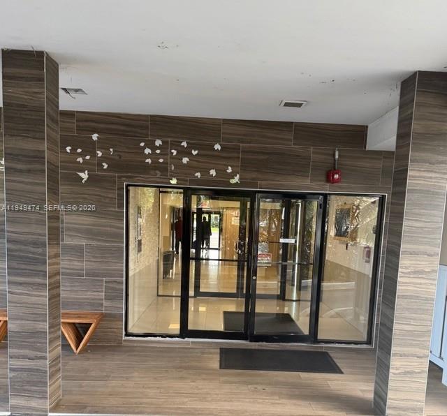 A building entrance features wood-look tiled walls, glass double doors, and a small wooden bench — 4164 Inverrary Dr # 913, Lauderhill FL 33319, LAUDERHILL, FL
