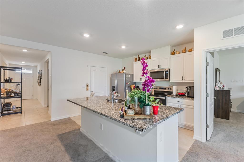 A kitchen features white cabinets, granite countertops, a central island, and stainless steel appliances — 1102 TUPELO TRAIL, HAINES CITY, FL