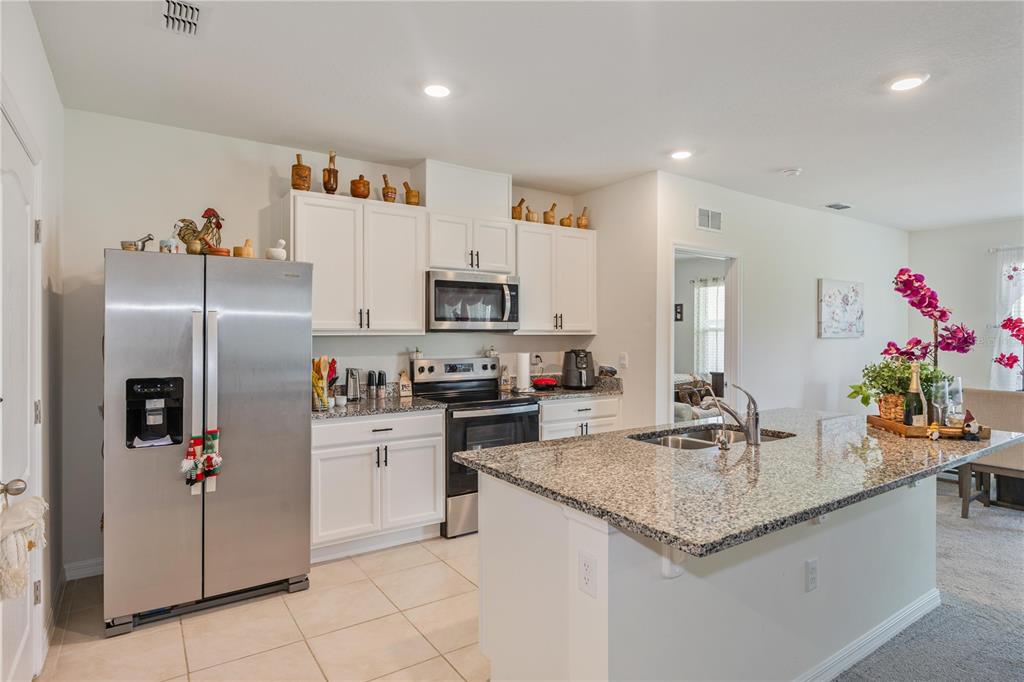 A kitchen features white cabinetry, stainless steel appliances, granite countertops, and a central island — 1102 TUPELO TRAIL, HAINES CITY, FL