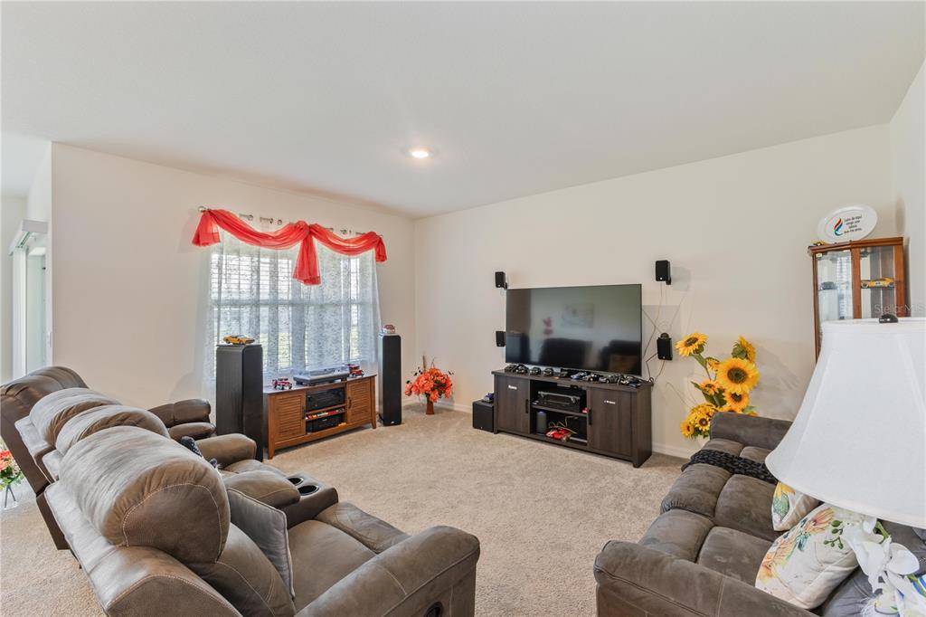 A living room features gray reclining sofas, a television on a media console, and carpeting — 1102 TUPELO TRAIL, HAINES CITY, FL