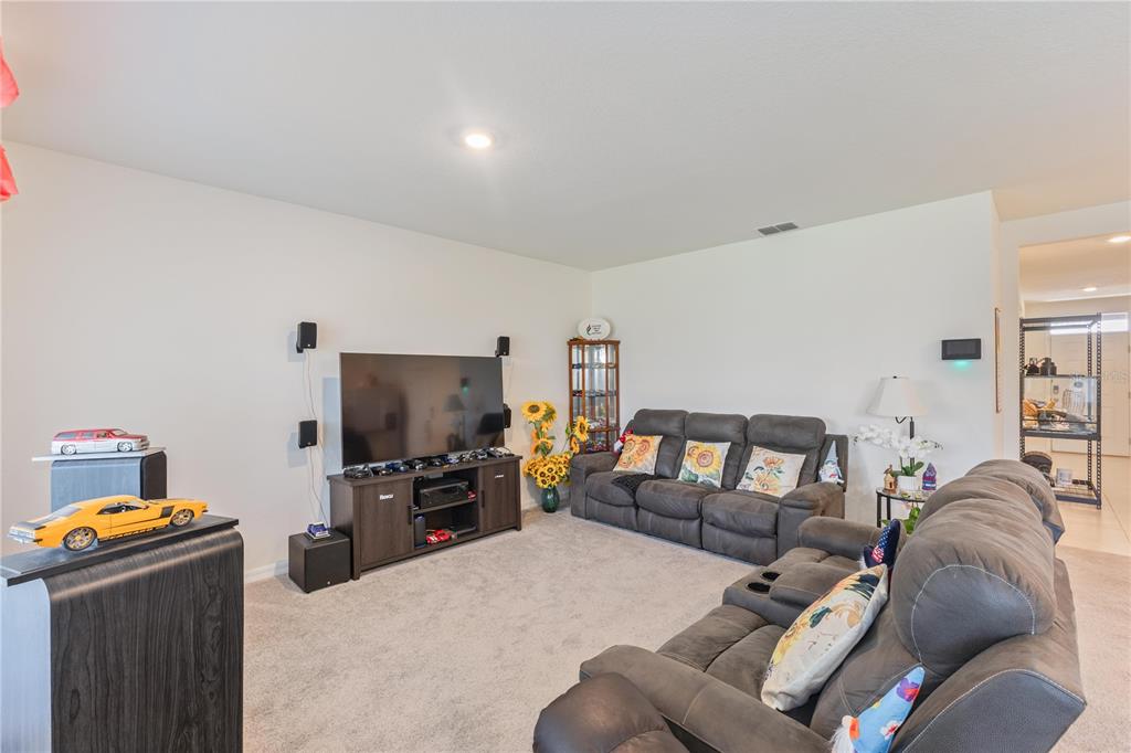 A living room features gray carpet, a dark entertainment center with a television, and sofas — 1102 TUPELO TRAIL, HAINES CITY, FL