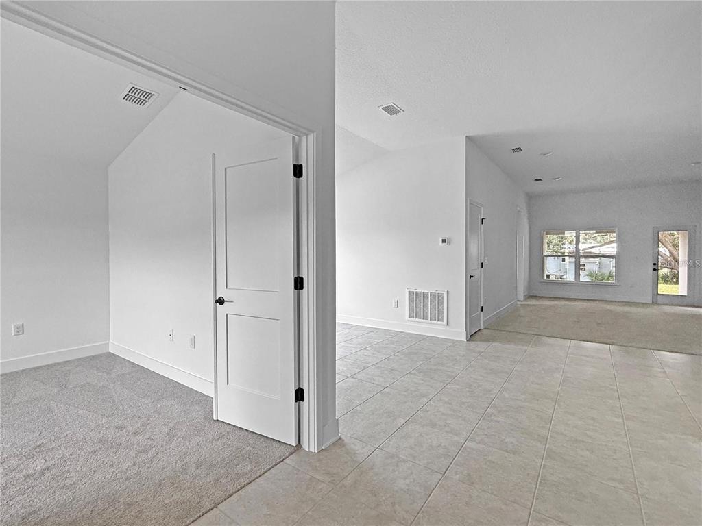 A room with gray carpet transitions into a tiled living area with white walls — 1654 ANN ROSE WAY, LEESBURG, FL