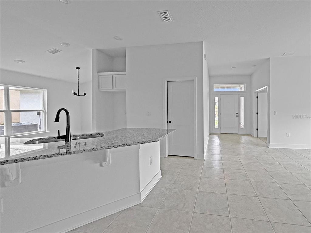 A kitchen island with granite countertops sits in an open-concept room with tile flooring — 1654 ANN ROSE WAY, LEESBURG, FL