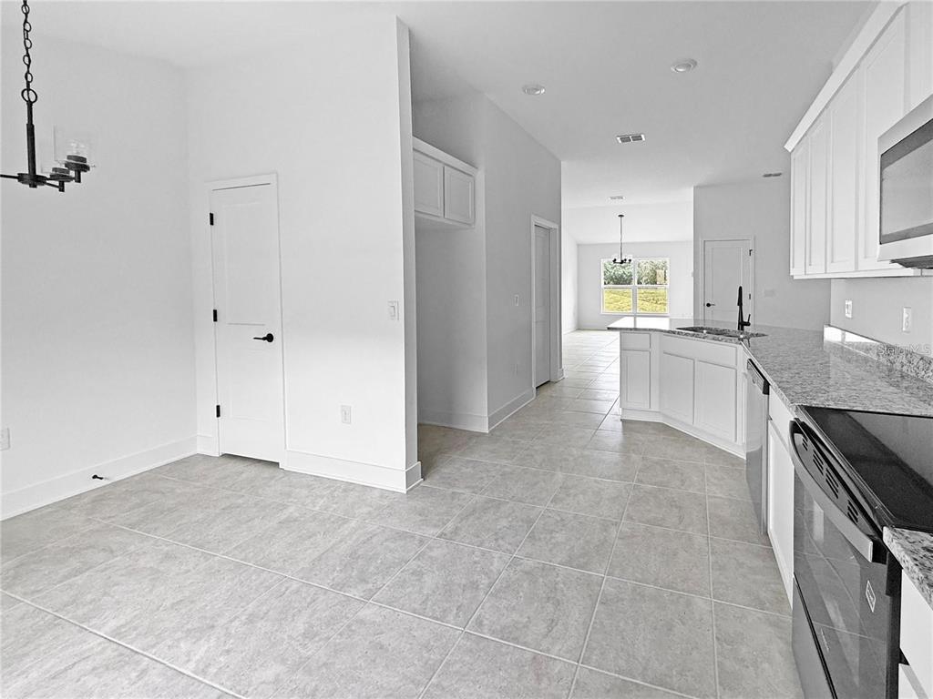 A kitchen with white cabinets, granite countertops, and tile flooring opens to a dining area — 1654 ANN ROSE WAY, LEESBURG, FL