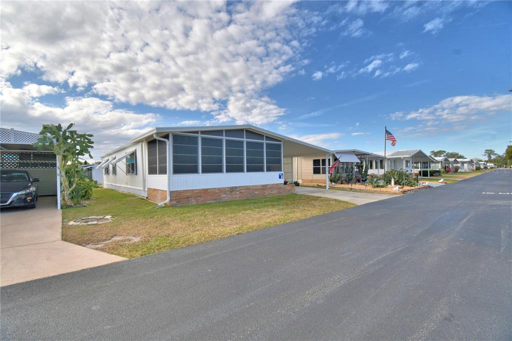 A manufactured home with a screened-in porch and attached carport sits along a paved street — 4228 CEDARWOOD STREET, WINTER HAVEN, FL