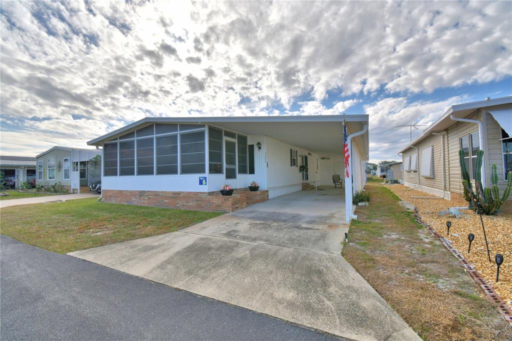 A single-story manufactured home with a screened-in porch, brick skirting, and an attached carport — 4228 CEDARWOOD STREET, WINTER HAVEN, FL