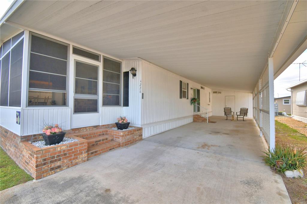 A white mobile home exterior features a large carport, a screened porch, and brick steps — 4228 CEDARWOOD STREET, WINTER HAVEN, FL