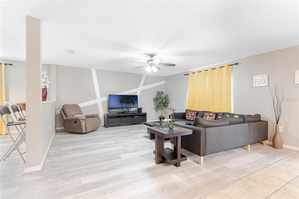 A living room features light wood-look flooring, a gray sectional sofa, and a television console — 4740 BLUE DIAMOND STREET, KISSIMMEE, FL