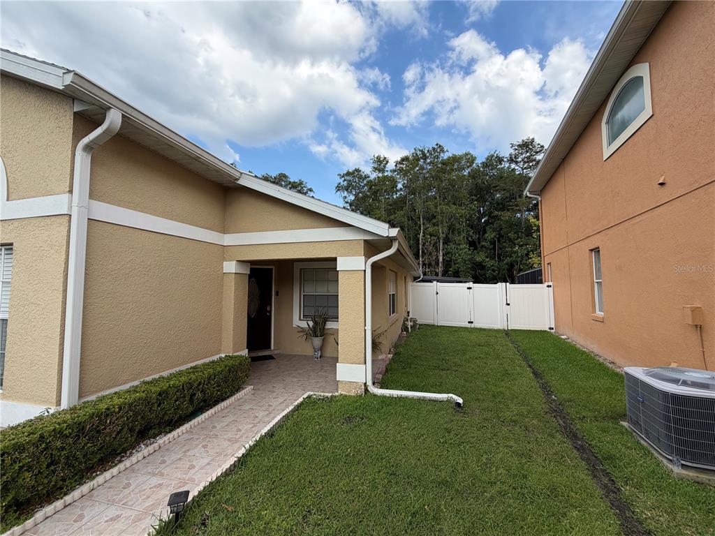 A side view of a tan house with a tiled walkway leading to the front entrance — 3264 FAIRFIELD DRIVE, KISSIMMEE, FL